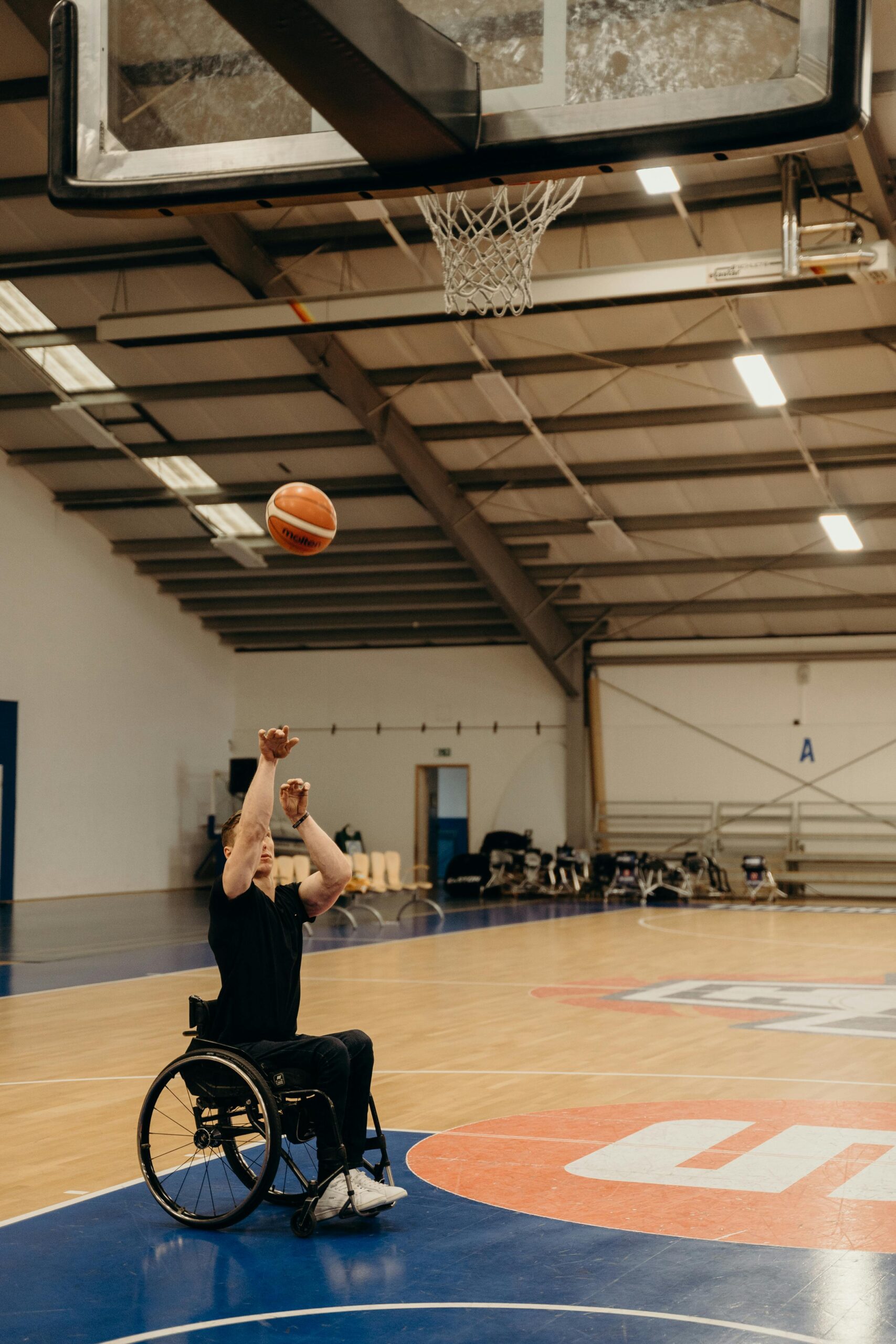 A wheelchair basketball player focuses intently as he shoots towards the hoop inside a sports hall.