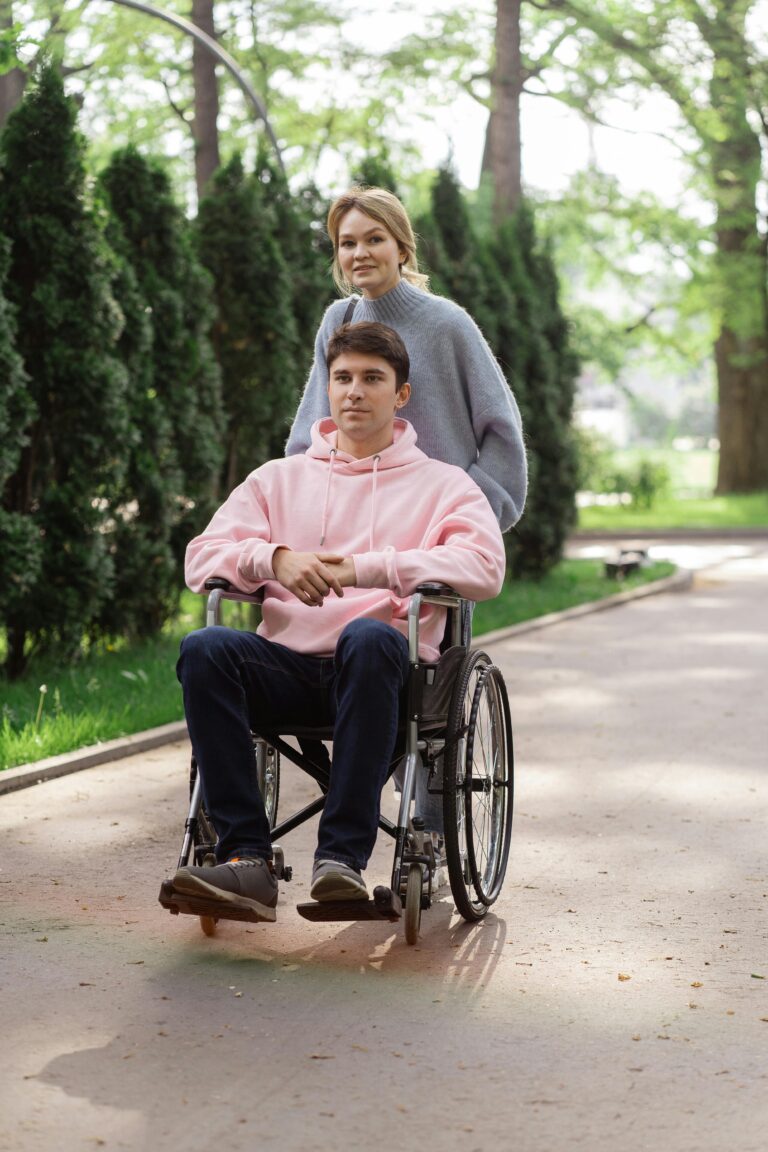 A young woman pushes a man in a wheelchair, enjoying a sunny day outdoors.